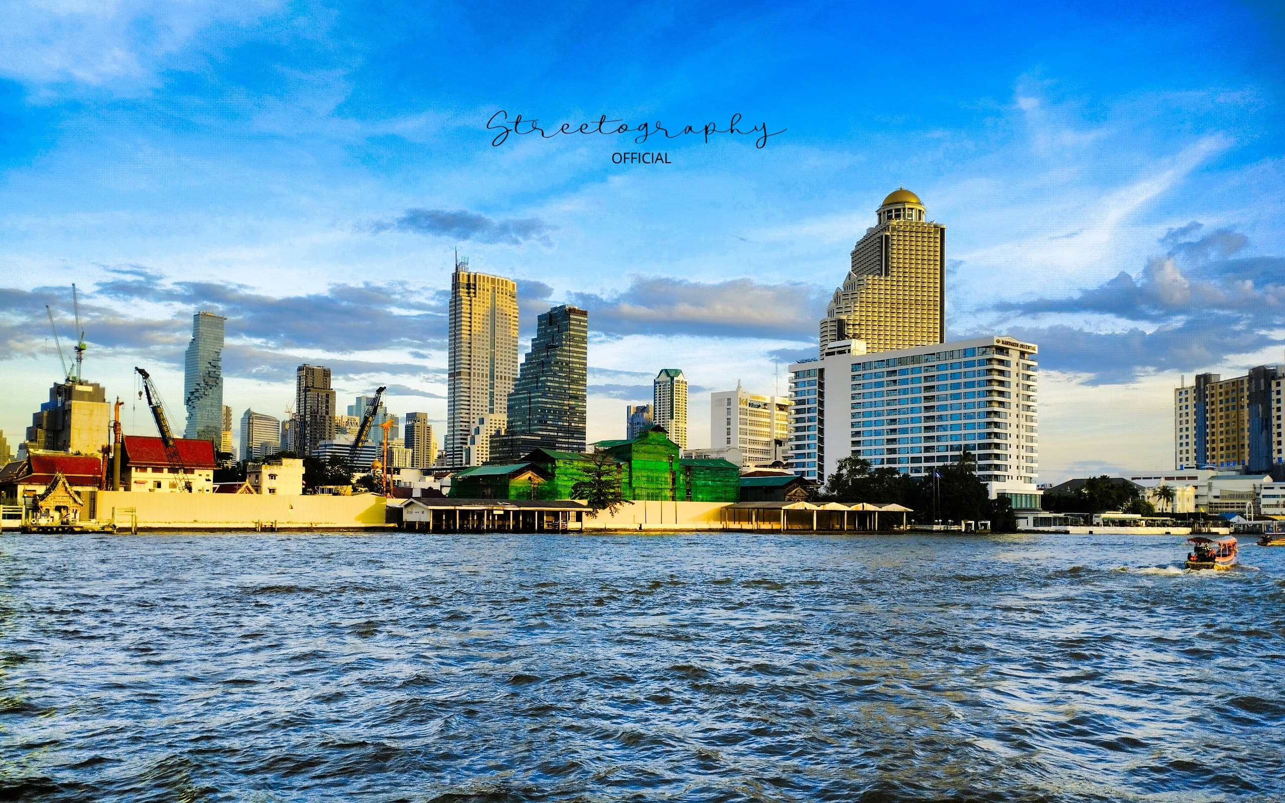 Bangkok skyline across the Chao Phraya River with modern towers and a small boat on the water